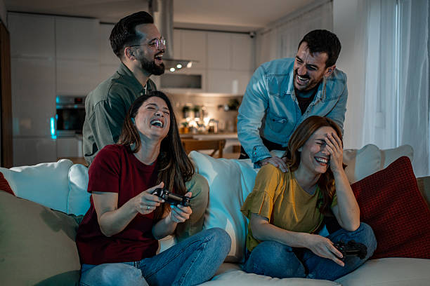 Friends laughing and bonding on a living room couch, playing video games together at night, enjoying casual leisure, togetherness and modern relaxed home entertainment