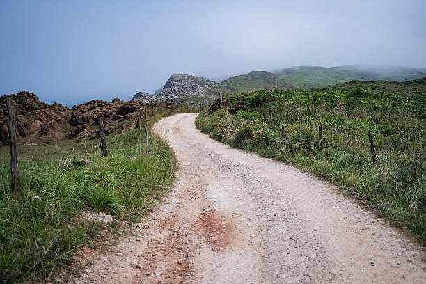 Curved dirt path in the countryside with morning fog, captured along the Camino de Santiago in Asturias, Spain. A tranquil rural landscape symbolizing travel, spirituality, and the journey of pilgrims.