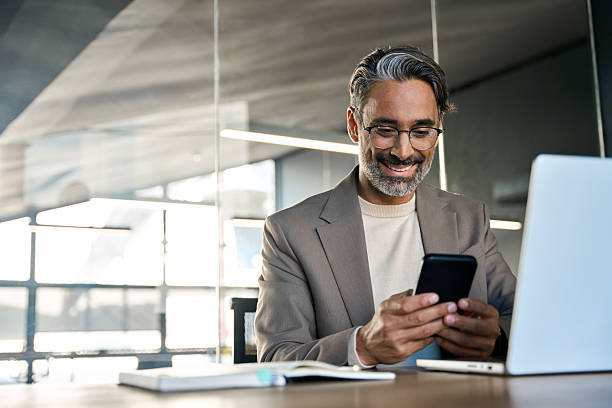 istock Smiling middle aged business man sitting in office using mobile phone. 2237491115