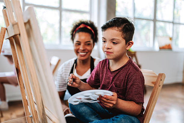 istock Boy with Down syndrome painting with help from art teacher 2237495206