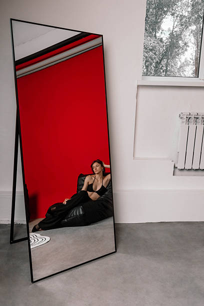 model poses on a black bean bag in a stylish studio with a vibrant red wall. large mirror captures her relaxed expression, showcasing the contemporary interior