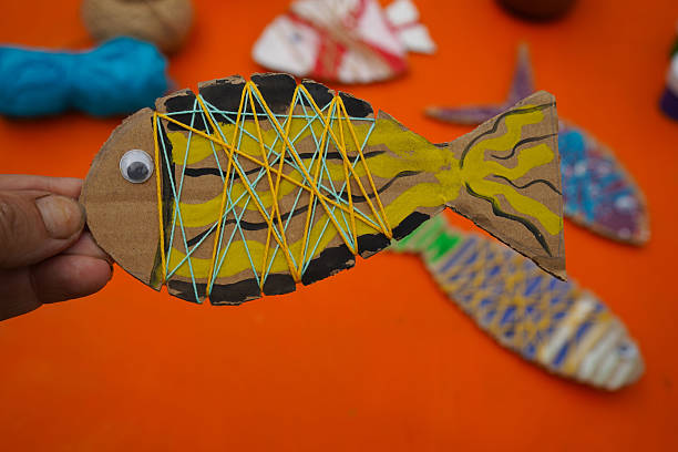 istock Construct a fish figure from cardboard, thread, and paint, with detailed steps, set against an orange background. 2237512288