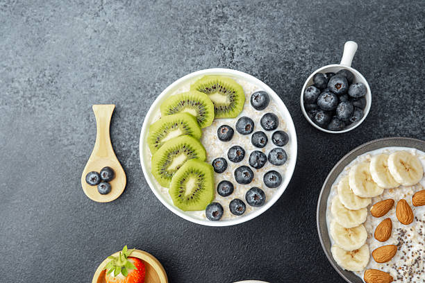 Topview of oatmeal bowl with kiwi and blueberries with assorted fruit on black table