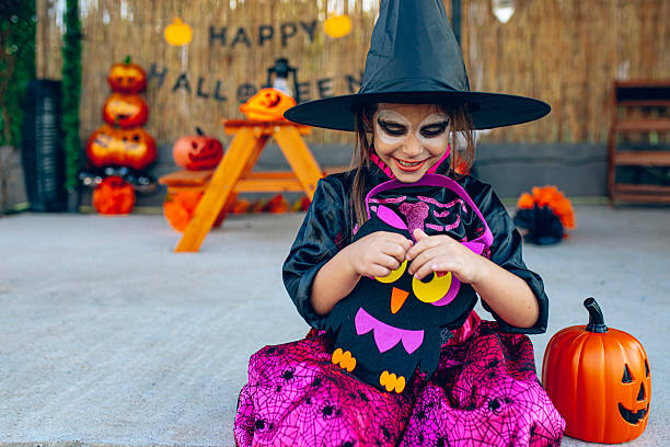 Young girl in a witch hat and costume posing outdoors during a Halloween celebration