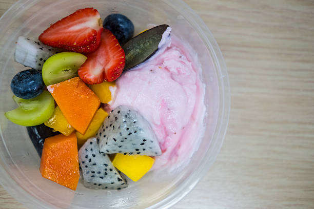 Strawberry greek yogurt topping with tropical fruit served in plastic bowl