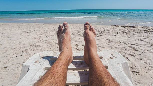 A man's legs with sand on them on a sunbed on a sandy beach. Relaxation on a beach. Man's legs with sand on them