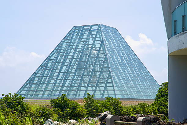 A faceted glass pyramid pavilion with a spherical sculpture inside anchors the Phoenix Island resort at Seopjikoji, framed by low coastal vegetation.