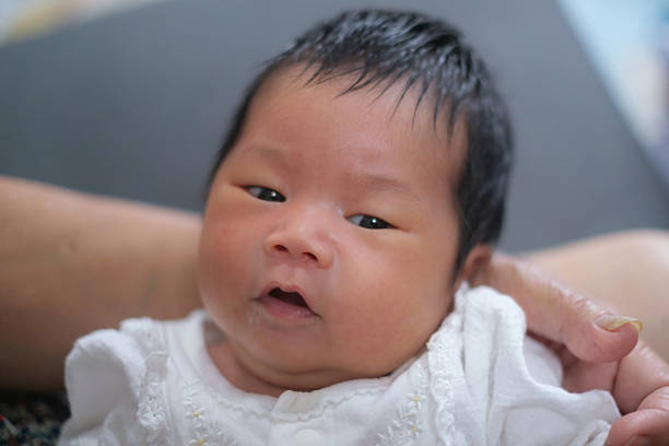 A newborn baby is playing on his mother's lap and looking around in confusion.