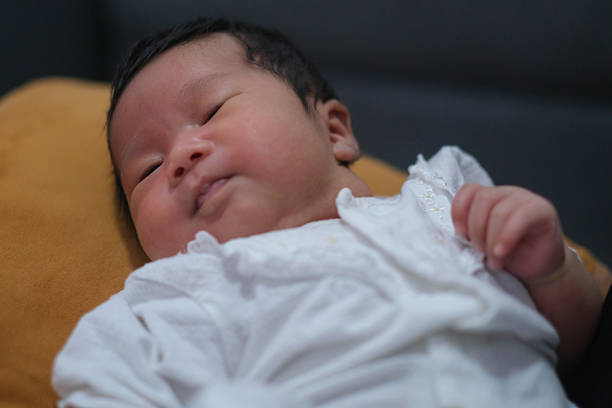A newborn baby is playing on the bed and raising his arms to show his happiness.