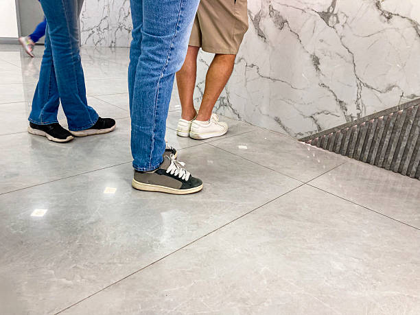 Line of people at the ticket office, detail of legs on a ceramic floor with reflections. Unrecognizable people.