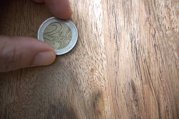 A hand holds several Euro coins on a green background. The shot highlights the metallic shine of the coins and their details.