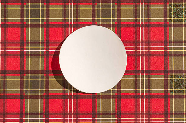 istock Round white placemat on red and brown plaid pattern background 2237541547
