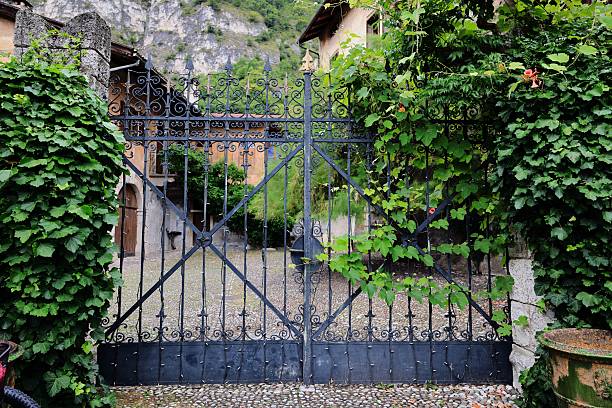 Ornate wrought iron gate adorned with lush green ivy, set against a rustic stone courtyard in a European village.