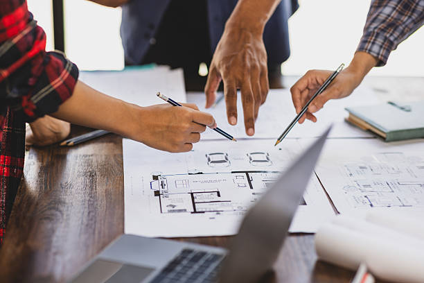 istock Architects and engineers are pointing at building plans and discussing over a model house, collaborating on a construction project. 2237543564