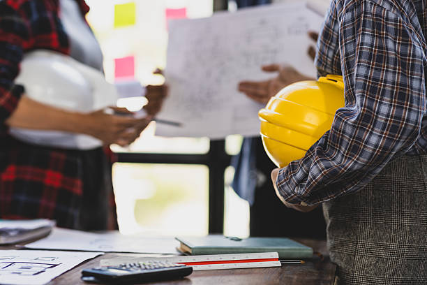 istock Architect holding yellow hardhat while attending a meeting with coworkers discussing blueprints and architectural plans in the office. 2237543589
