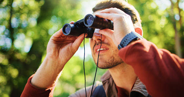 istock Explore, hike and man in forest with binocular, bird watching or sightseeing in holiday hobby. Observation, nature and tourist in woods with field glasses, outdoor or animal search on solo trip. 2237546944