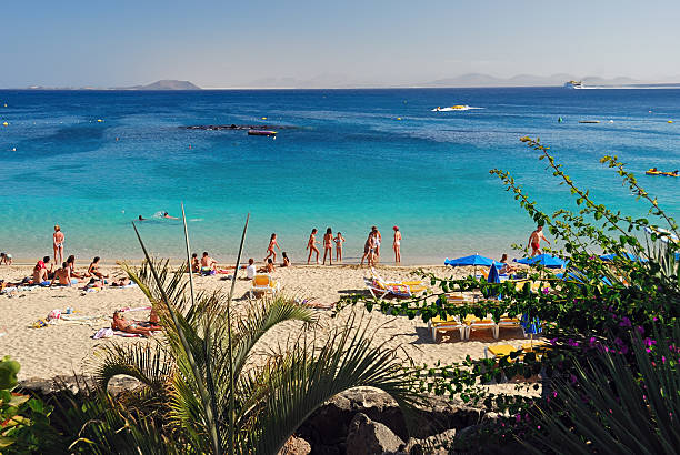 Playa Blanca, Spain - Jun 24, 2008: Tourists relax on famous beach in Playa Blanca on Lanzarote island, Atlantic ocean and Fuerteventura island on background