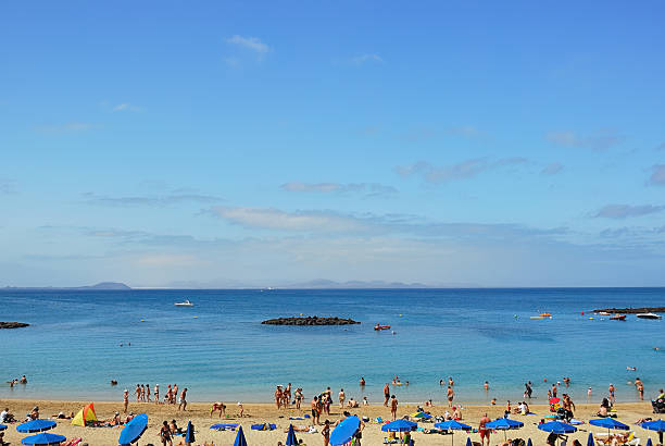 Playa Blanca, Spain - Jun 25, 2008: Tourists relax on famous Dorada beach in Playa Blanca on Lanzarote island, Atlantic ocean and Fuerteventura island on background