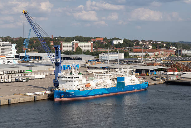 Kiel, Germany-August 9, 2025: LNG bunkering vessel Kairos docked at port terminal, surrounded by cranes, warehouses and parked trucks in background.