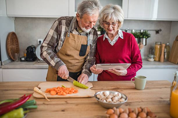 istock Happy senior couple enjoying time in the kitchen. He chops vegetables while she reads instructions from a recipe app 2237557031