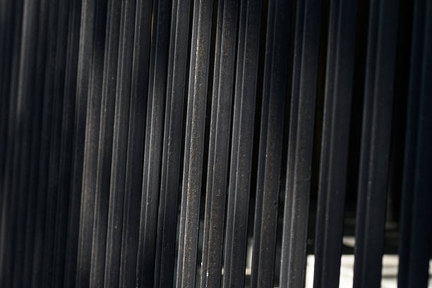 A close-up photograph captures the repeating vertical lines of a dark metal fence, creating an abstract and textural background. The composition emphasizes depth and perspective with a soft focus, ideal for backgrounds and architectural concepts.