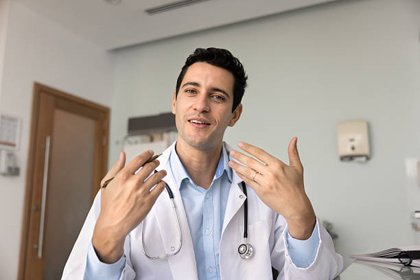 Handsome young Hispanic GP doctor man talking on video conference call, looking at camera, speaking from screen, giving online consultation, telehealth support. Head shot portrait