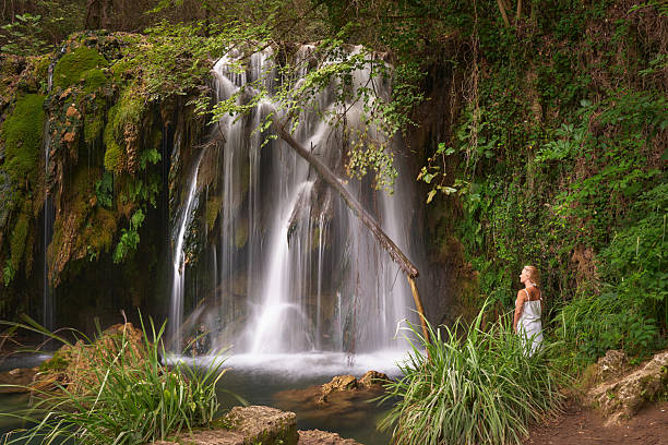 Young adult woman enjoying tranquil nature by a flowing waterfall.