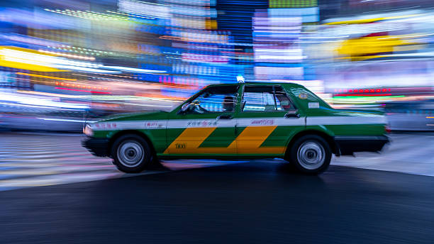 A Green taxi speeds through the streets of Tokyo at night in the rain with a backdrop of neon lights. May 2025