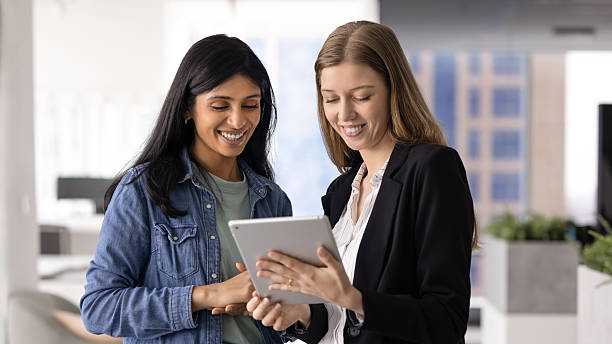 istock Two happy diverse female office friends using gadget together 2237574886