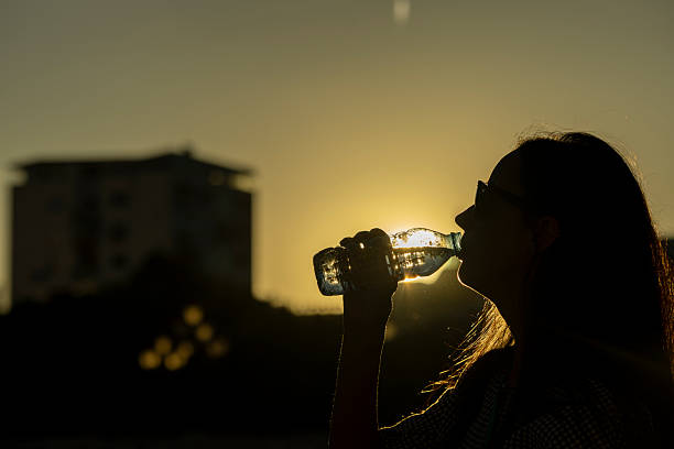Silhouette of a woman drinking water with sunset reflection