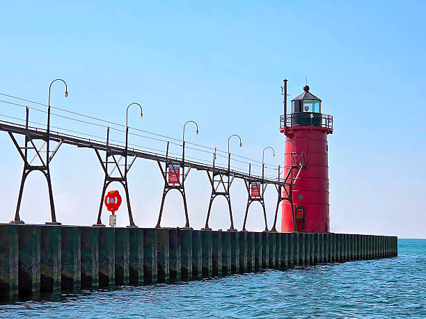 A vibrant red South Haven lighthouse in Michigan stands tall at the end of a pier, contrasting against the clear blue sky
