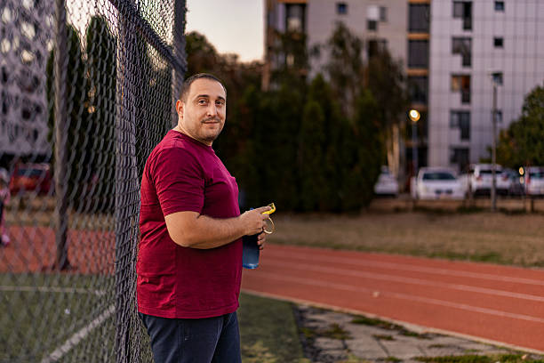istock Overweight man taking a break of training while standing leaning on the  on the hedge on the sports track 2237580205