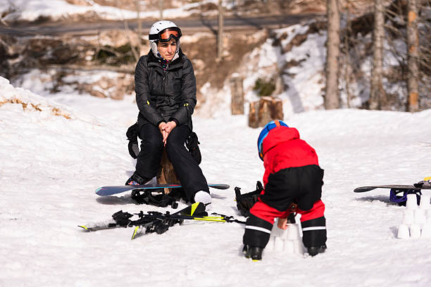 istock Snowboarder watching child playing in snow on mountain top 2237585082
