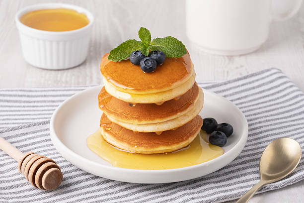 istock Stack of fluffy pancakes with blueberries and honey on a cozy breakfast table in soft morning light 2237601898