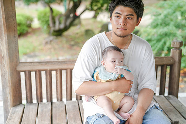 A man is holding a baby on a bench. The baby is wearing a blue shirt and a blue bib