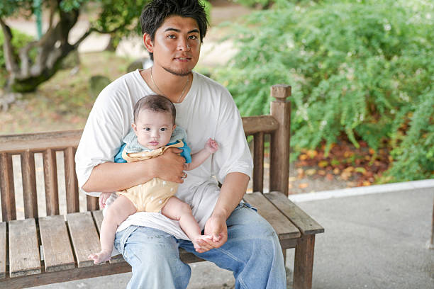 A man is holding a baby on a bench. The baby is wearing a yellow outfit. The man is smiling and seems to be enjoying the moment