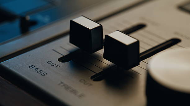 Macro view faders on vintage sound recorder in professional studio. Closeup bass treble sliders stay still at retro musical console indoors. Old style recording equipment panel under soft light.