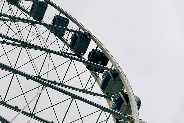 Low angle view of a massive metal and glass ferris wheel, specifically the Seattle Great Wheel. Taken on the Seattle Waterfront in Washington State on an overcast day in summer.