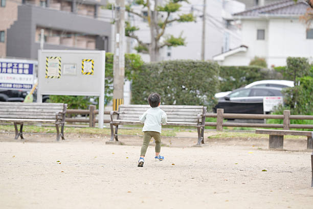 A young boy runs through a park with a sign in the background that says \