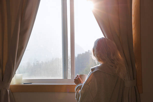 istock Woman enjoys hot beverage in front of window 2237619207