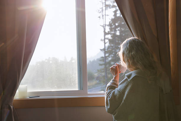 istock Woman enjoys hot beverage in front of window 2237619208
