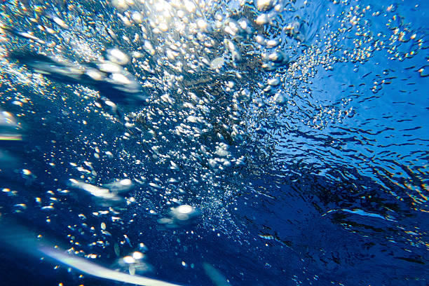Underwater image captured with a GoPro camera, showing rising air bubbles and sunlight penetrating the surface of a swimming pool. The deep blue water and dynamic reflections evoke freshness, motion, and clarity. Ideal for themes of wellness, summer, underwater photography, and recreational lifestyle. Suitable for commercial use where vibrant atmosphere and fluid detail are essential.