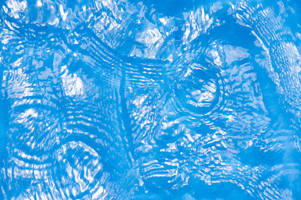 Blue water with ripples on the surface. Defocus blurred transparent blue colored clear calm water surface texture with splashes and bubbles. Water waves with shining pattern texture background.