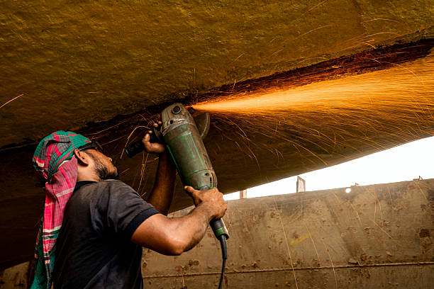 Dhaka, Bangladesh - 14 September, 2018: A construction worker operates a power grinder, cutting metal as bright sparks scatter across a dim indoor work site. The scene conveys skilled labor, safety, and intense focus during metalwork.