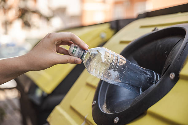 istock Hand placing a plastic bottle into a recycling container with yellow lid in an urban area. 2237656247