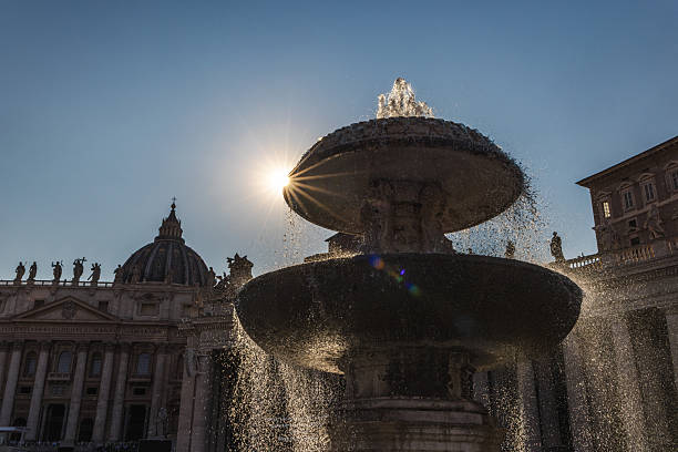 Fountain in St. Peter's Square with the sun shining dramatically through water streams, Vatican City landmark at sunrise. High quality photo