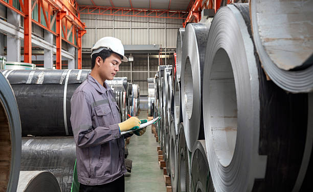 istock A worker dressed in hardhat and  protective glove, stand in a factory check material while holding document clipboard. The environment is organized with rolls of metal. 2237663953