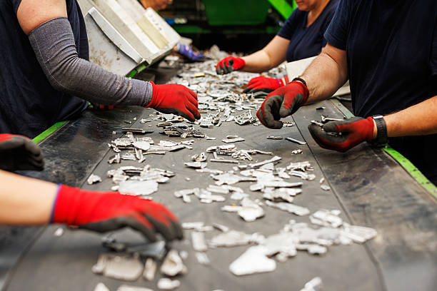Close-up view of hands in red gloves picking out metal fragments from a moving conveyor belt in a recycling facility