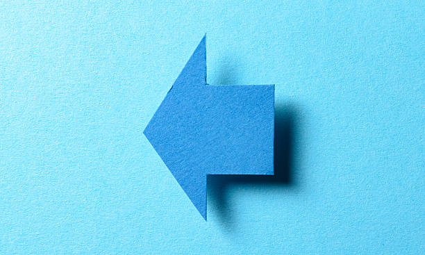 istock Blank paper cardboard arrow direction sign with shadow and copy space for text on blue background, flat lay top view pointing symbol conceptual message backdrop 2237668953