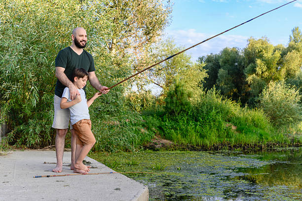 istock Father teaching son how to fish by riverbank. 2237669050